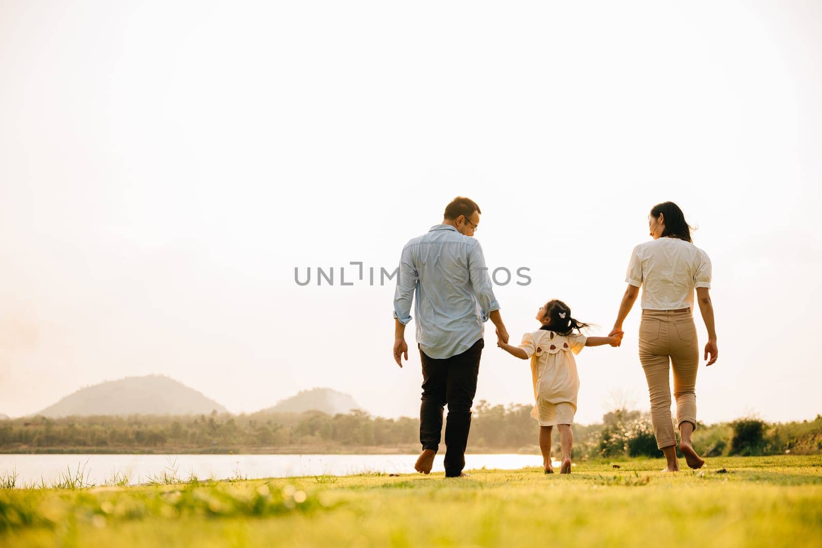 Back view of Happy Asian family walking and playing together in a scenic garden by Sorapop