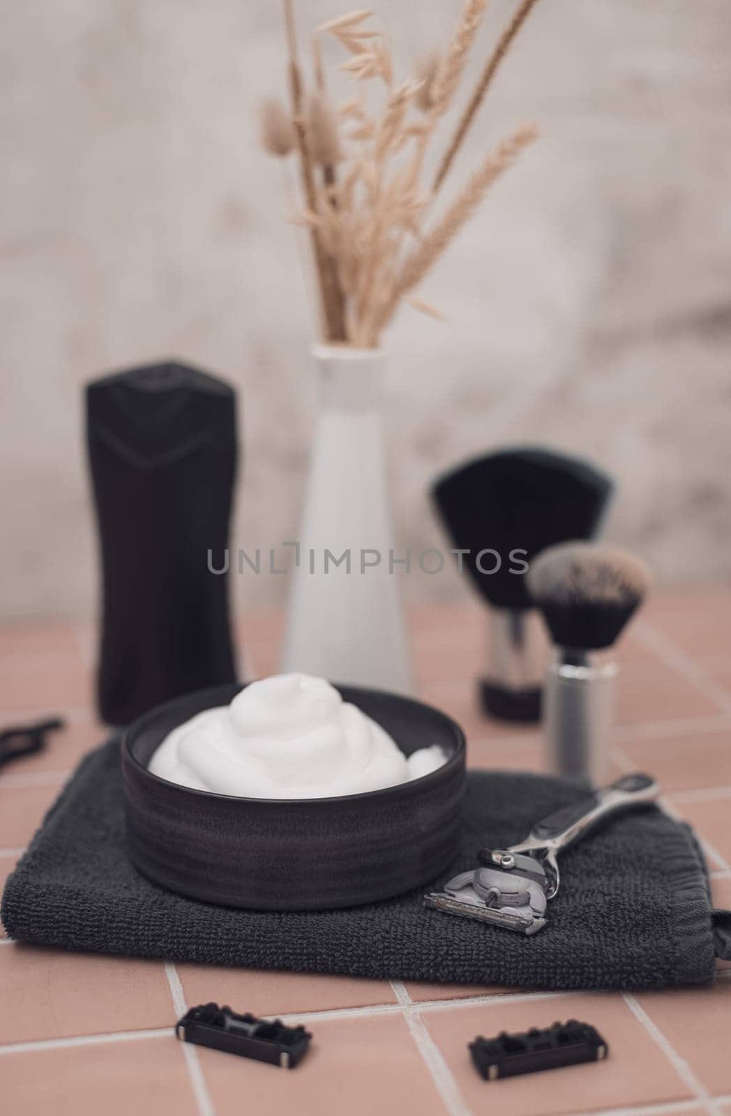 Shaving foam in bowl, shaving brush, razor, razor heads, scissors, bottle of aftershave cream and vase with dried flower on brick tiled background, close-up side view. The concept of a male hairdresser, beauty salon, beard shaving.