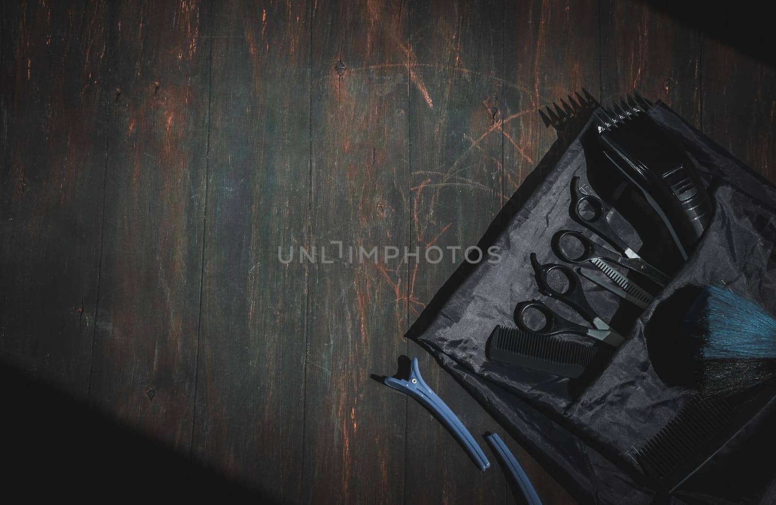 Scissors, combs, hair clipper, brush and clips with apron lie on the right on a black homemade wooden background with a little copy space on the left, flat lay close-up. The concept of a male barbershop, dark style.