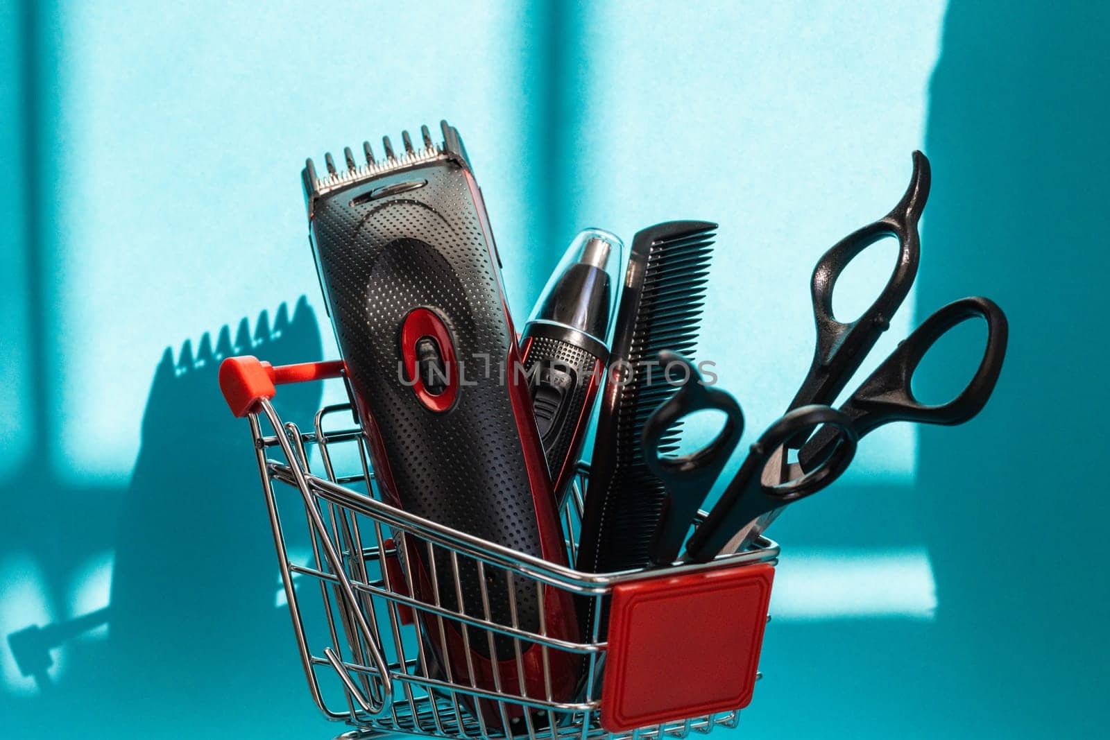 Hair clippers, two pairs of scissors and one comb lie in a mini basket on a blue background, close-up side view. The concept of hairdressing and shopping.