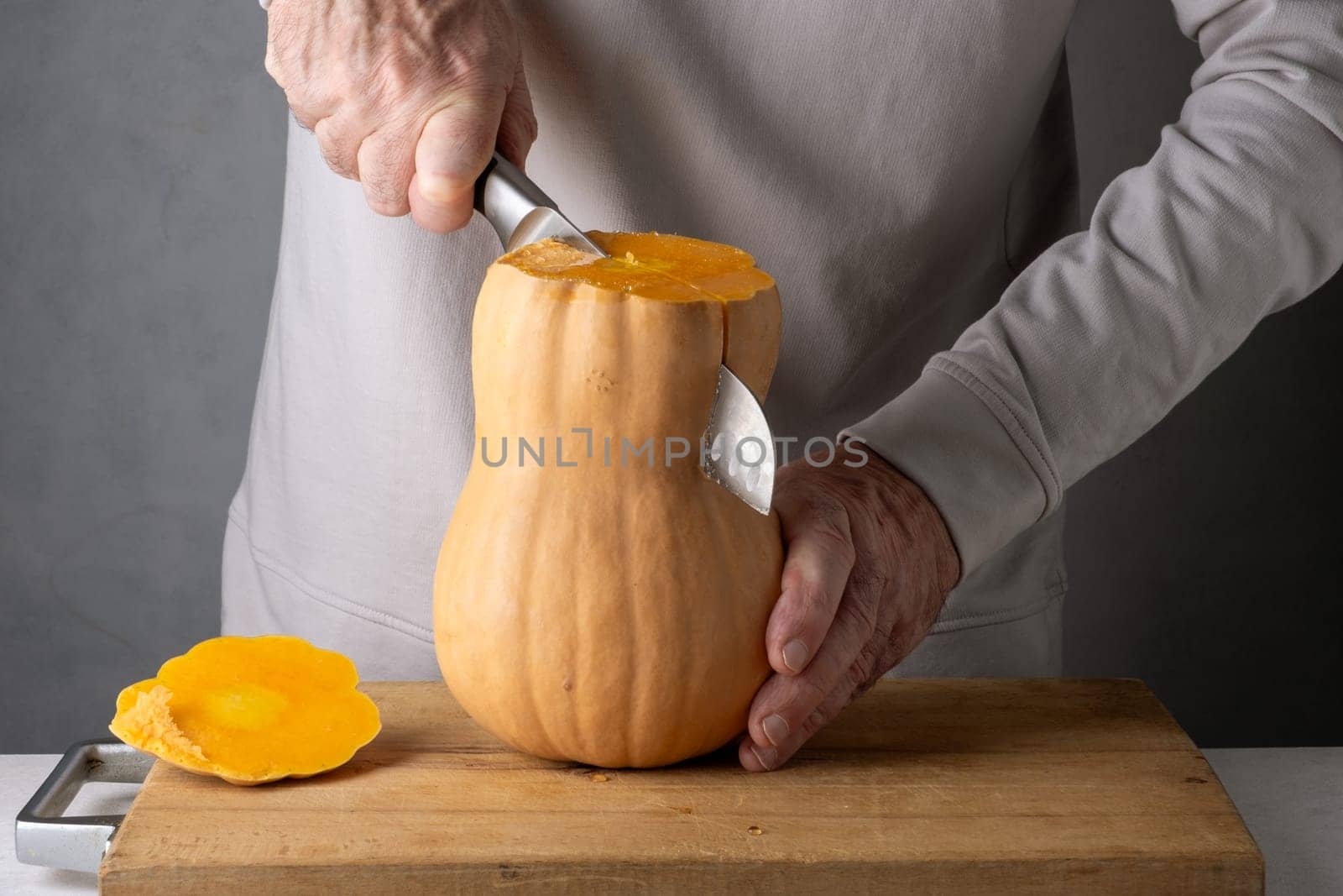 Caucasian unrecognizable middle-aged man cutting pumpkin on a wooden cutting board. Selective focus.