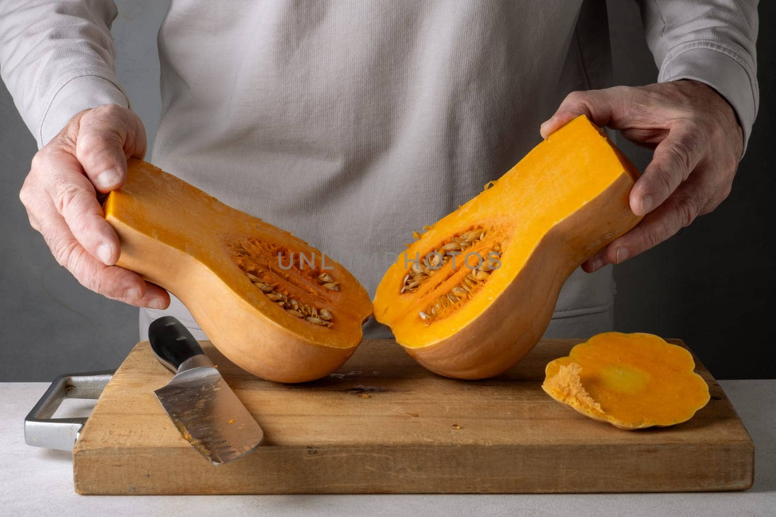 Caucasian unrecognizable middle-aged man cutting pumpkin on a wooden cutting board. Selective focus.