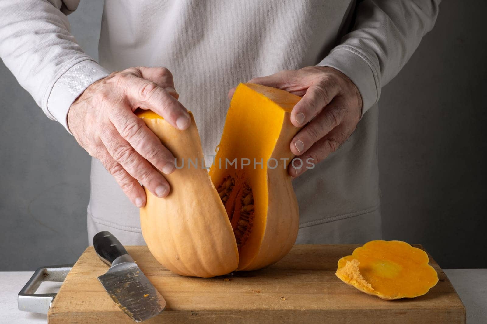 Caucasian unrecognizable middle-aged man cutting pumpkin on a wooden cutting board. Selective focus.