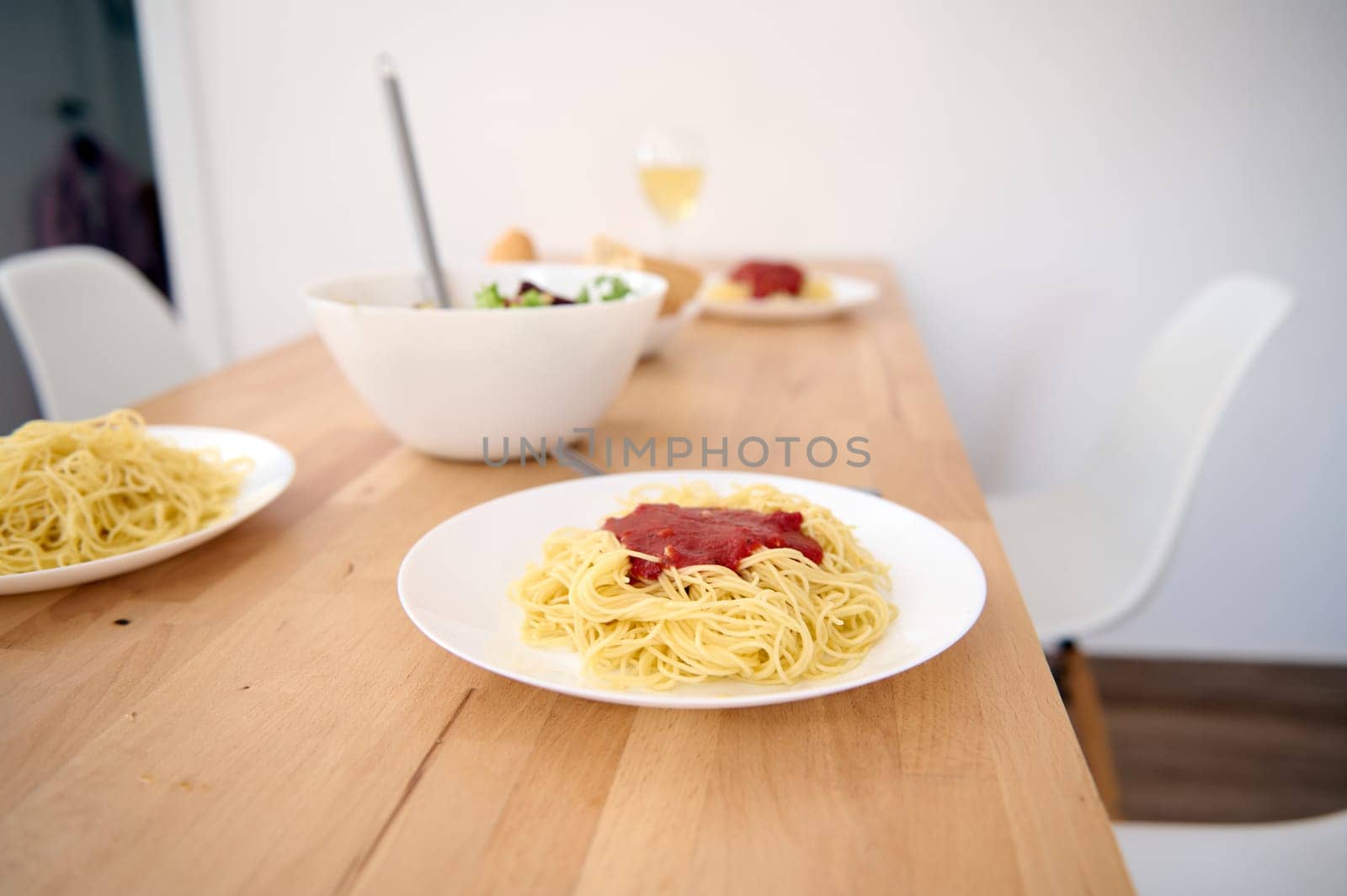 A wooden table with served dishes of freshly prepared Spaghetti with tomato sauce in modern light home kitchen interior. Food and drink concept. Healthy eating and dieting. Italian traditional cuisine