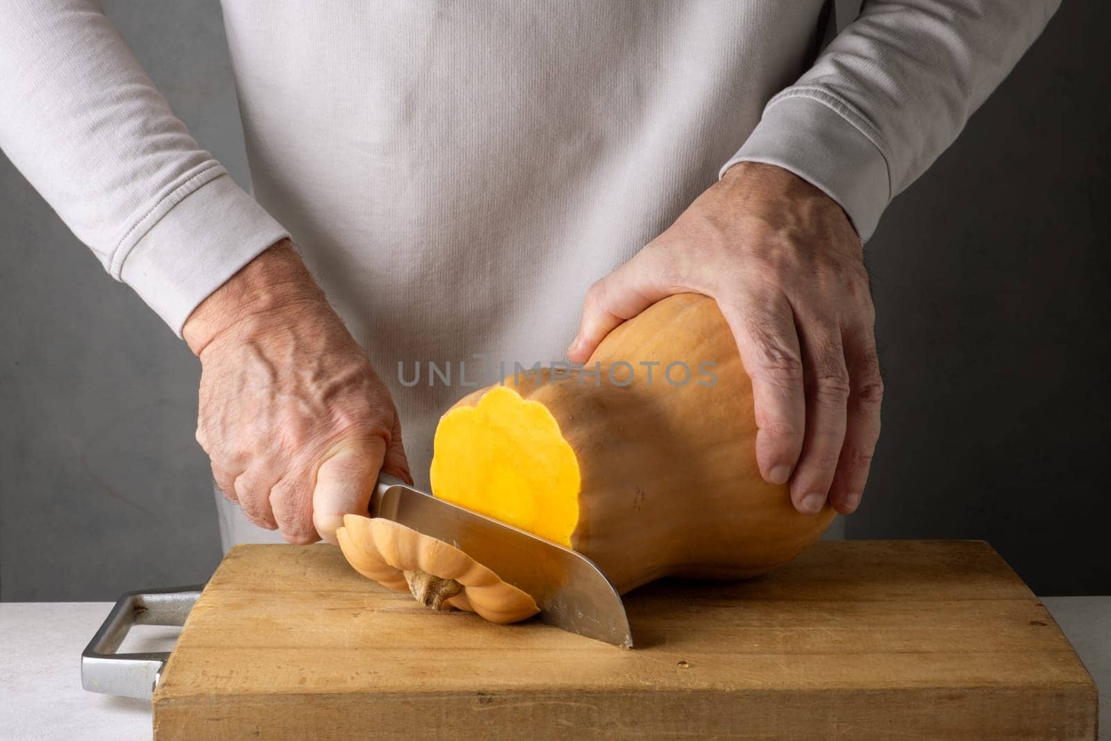 Caucasian unrecognizable middle-aged man cutting pumpkin on a wooden cutting board. Selective focus.