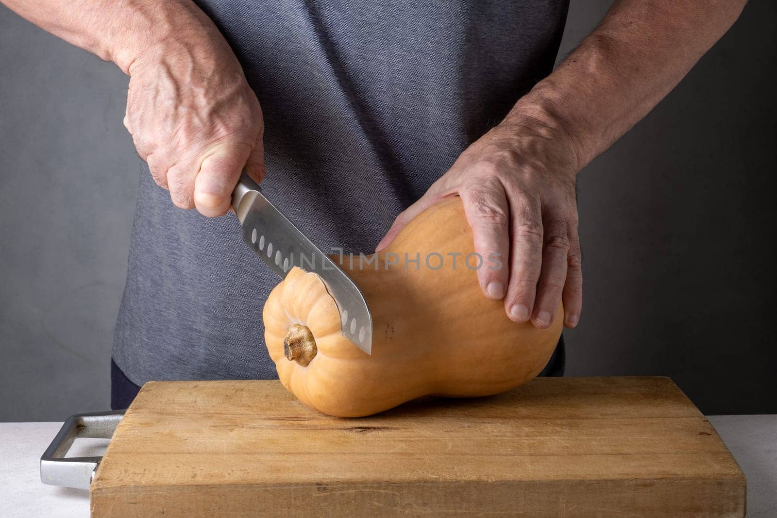 Caucasian unrecognizable middle-aged man cutting pumpkin on a wooden cutting board. Selective focus.