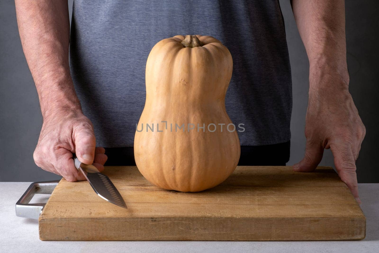 Caucasian unrecognizable middle-aged man cutting pumpkin on a wooden cutting board. Selective focus.