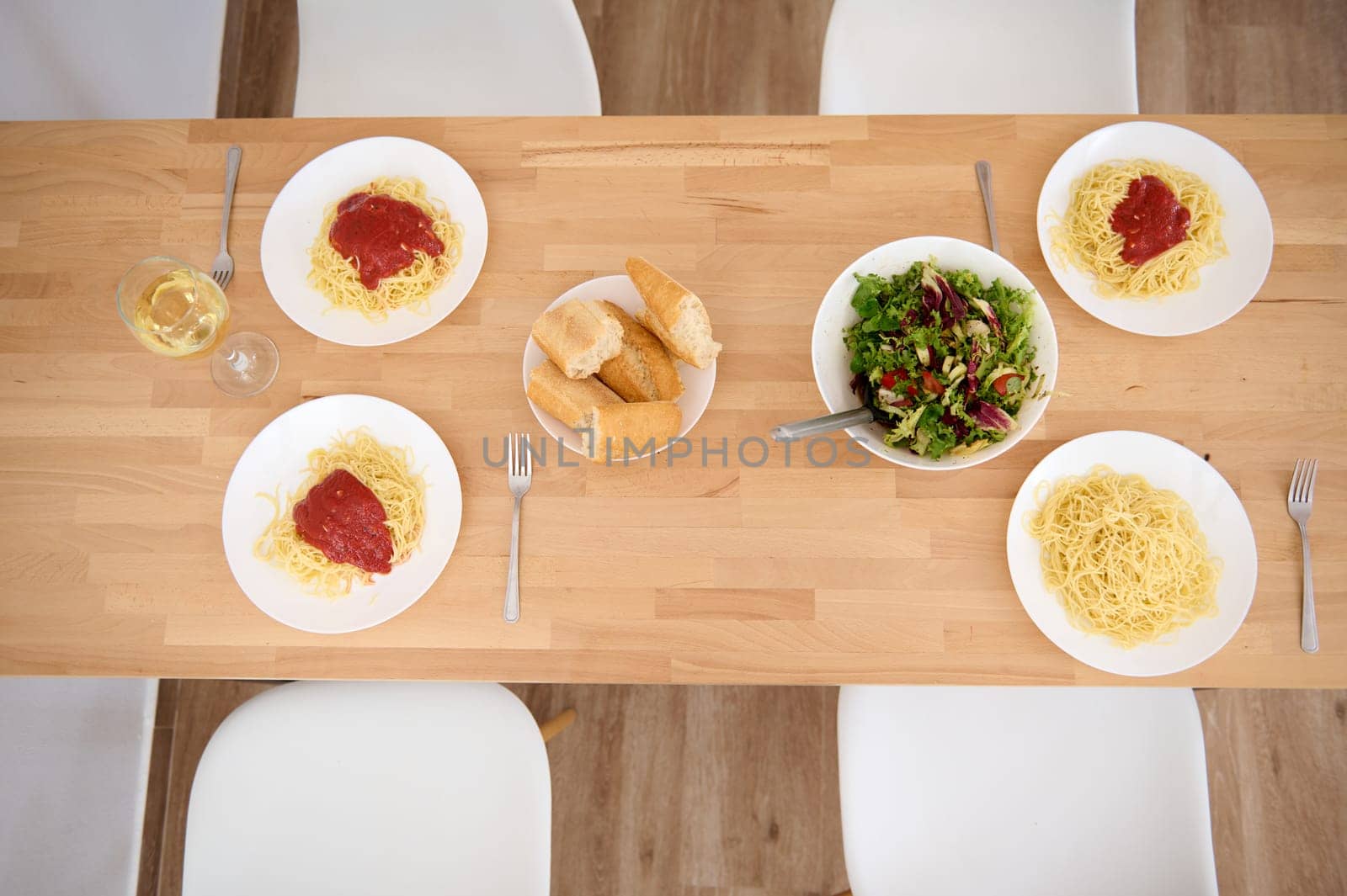 Top view of plates with appetizing spaghetti and classic tomato sauce, a wine glass of white wine and a bowl of fresh raw vegan salad on wooden table . Still life with traditional Italian food - pasta