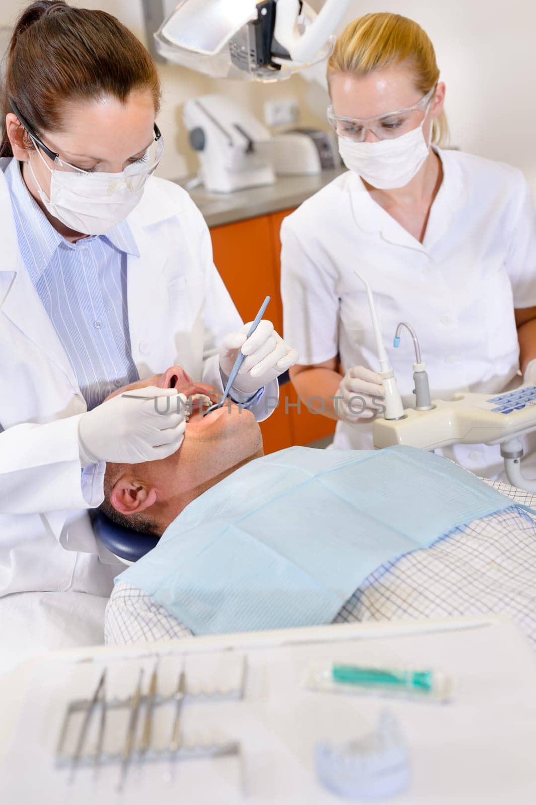 Female dentist and nurse doing operation on male patient