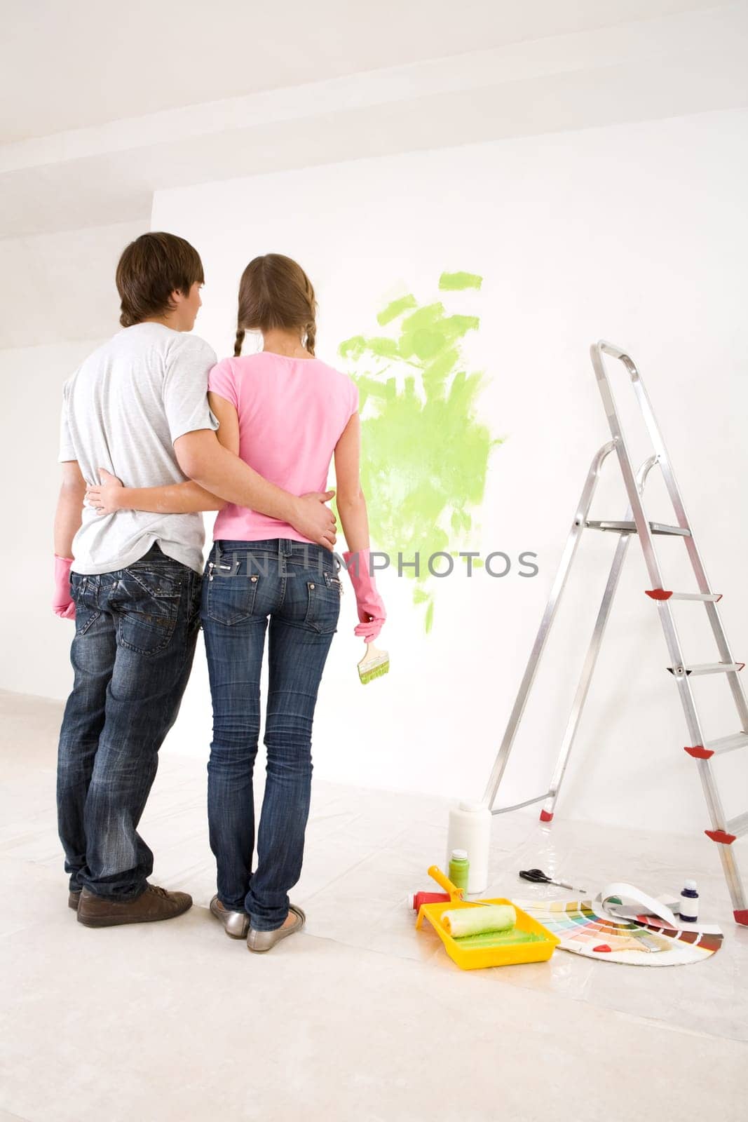 Rear view of embracing couple looking at wall with green paint on