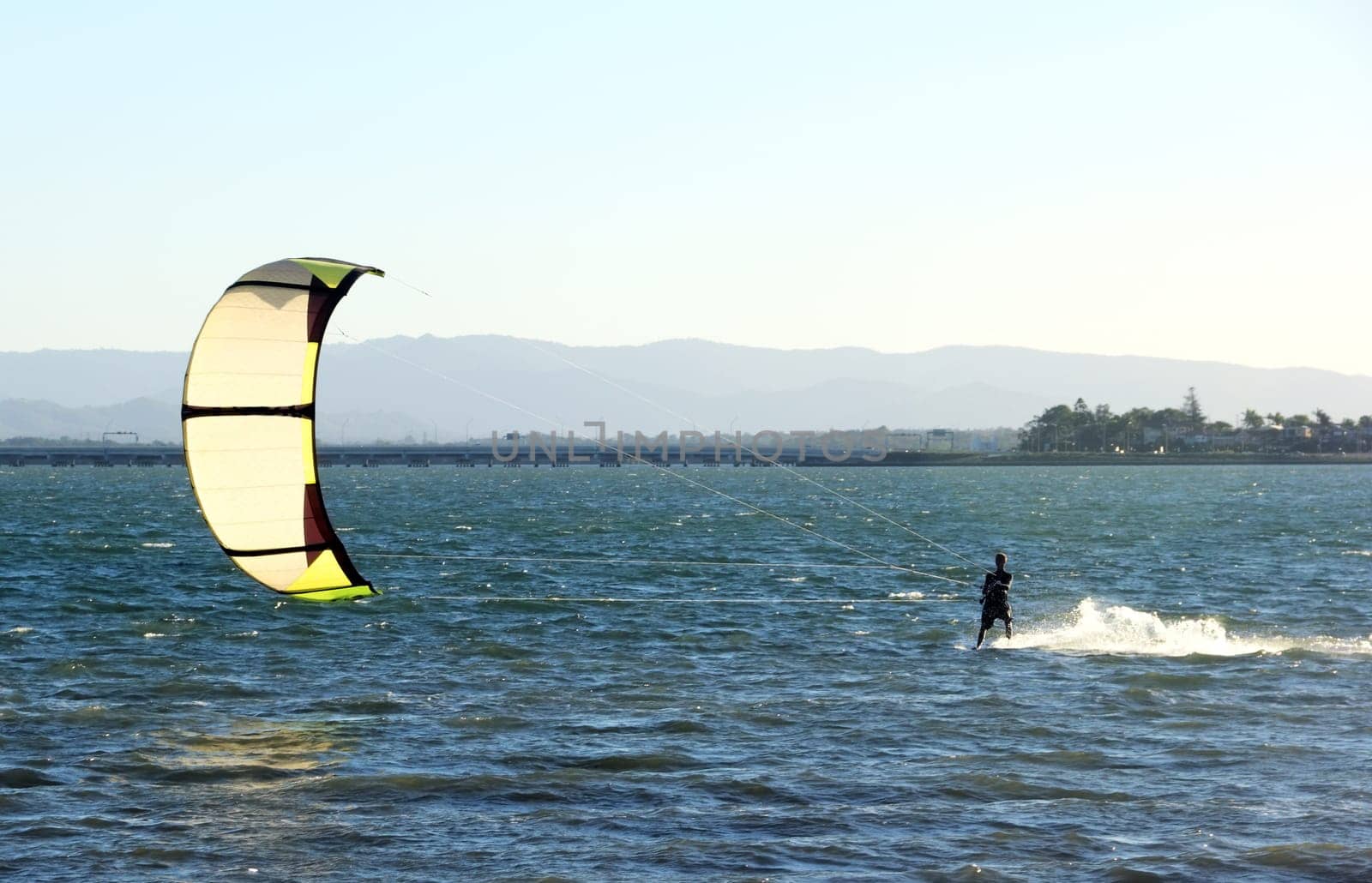 Kite surfer speeding across the water at sunset.