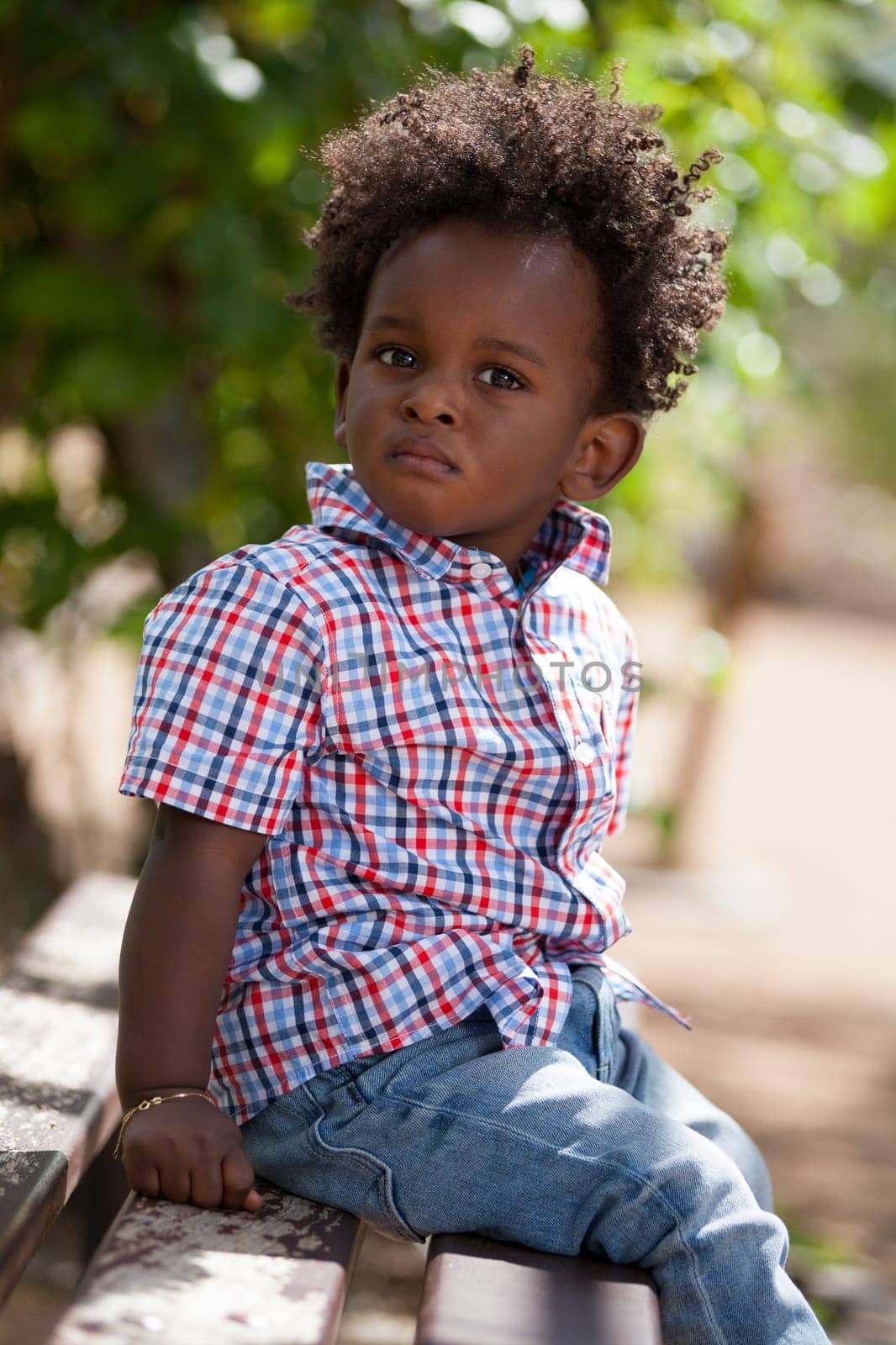 Outdoor portrait of a cute black baby boy sited on a bench