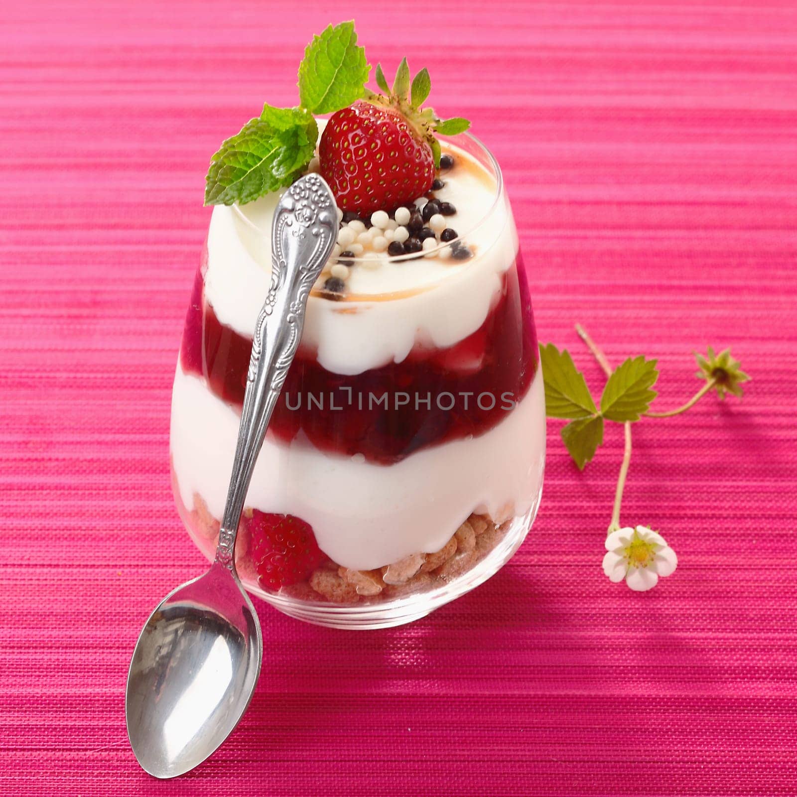 Individual serving of a gourmet strawberry dessert with layered cream alternating with fresh fruit and purée in a glass container