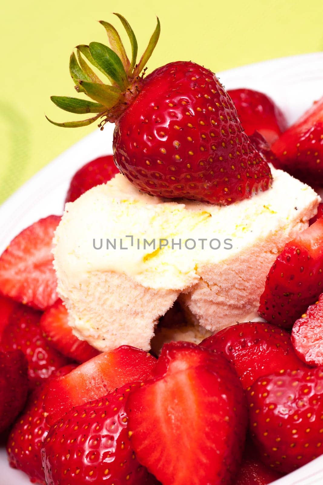 A red strawberry on vanilla ice cream against a yellow-green background