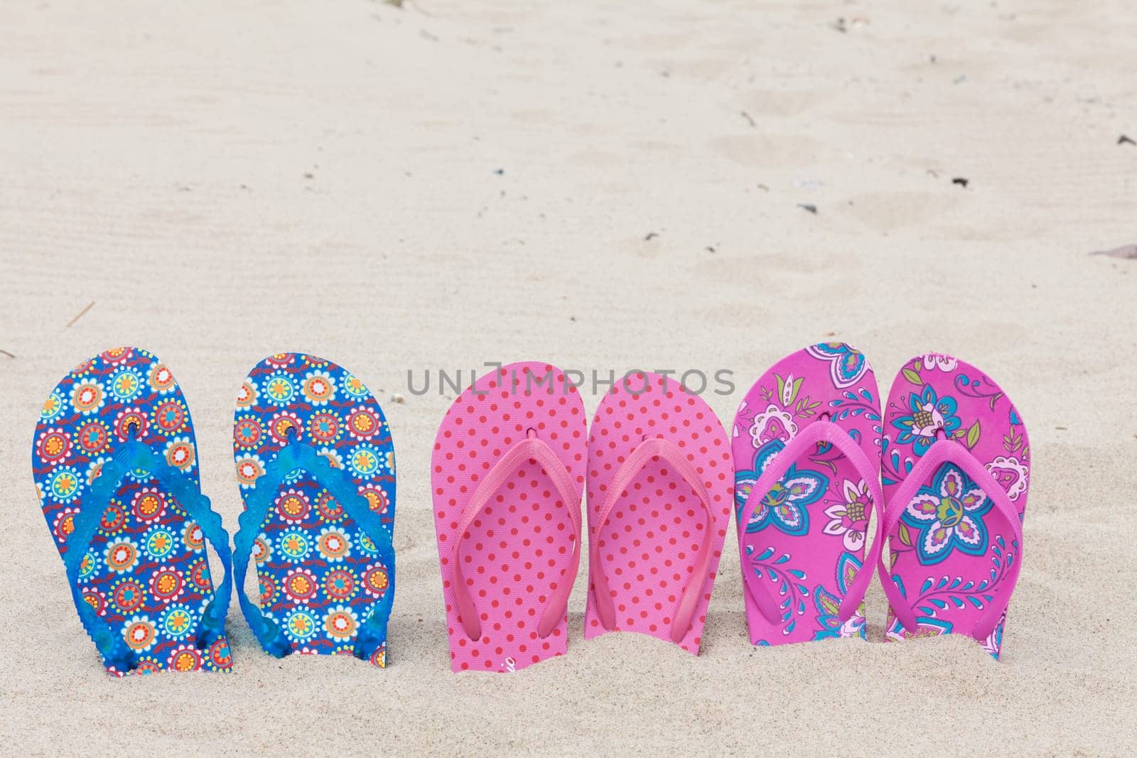 Three pairs of flip-flops on the sandy beach