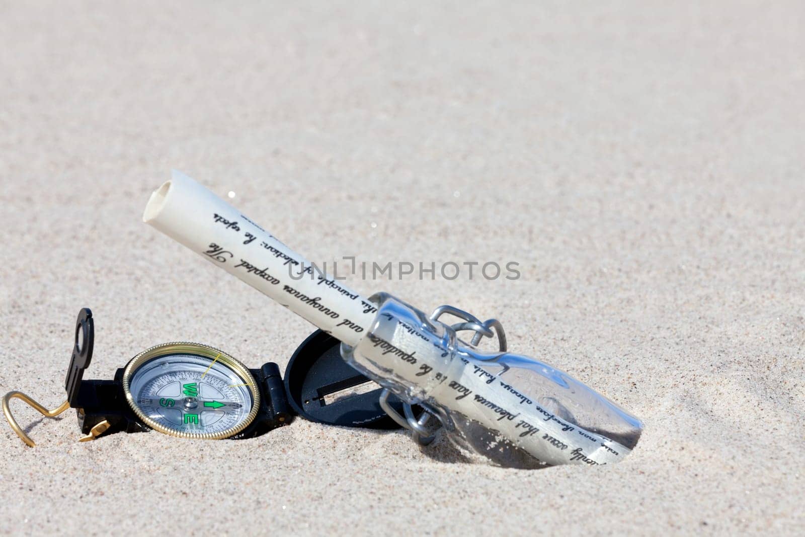 Message in a bottle with letter and compass in the sand