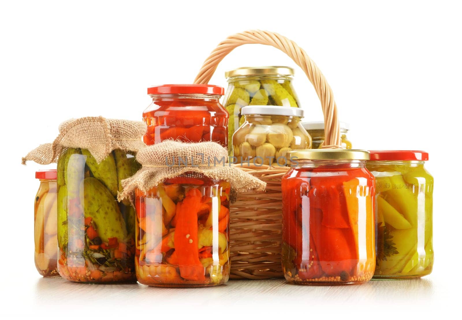 Composition with wicker basket and jars of pickled vegetables. Marinated food.