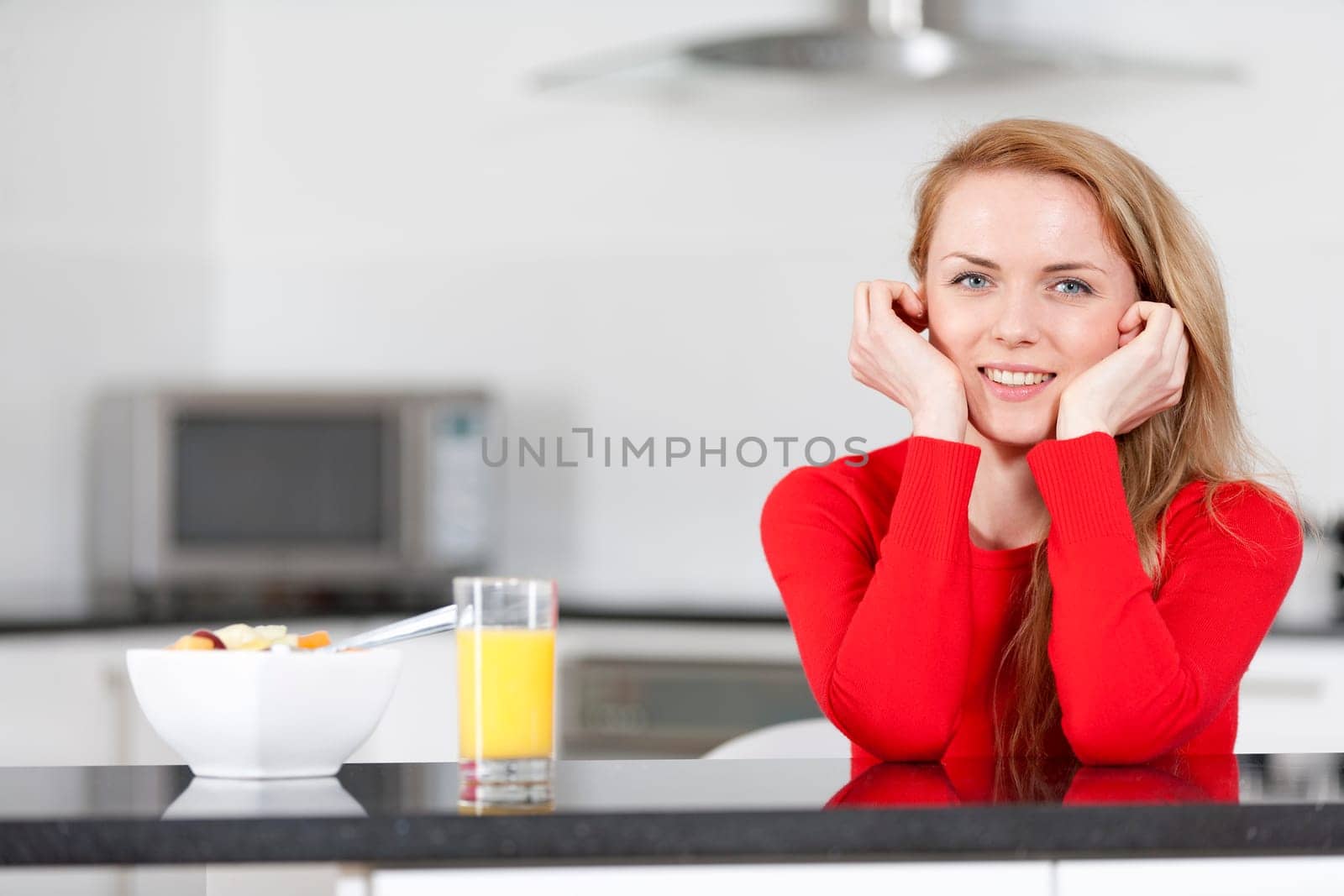 Young woman enjoying a bowl of fresh fruit in her kitchen with orange juice