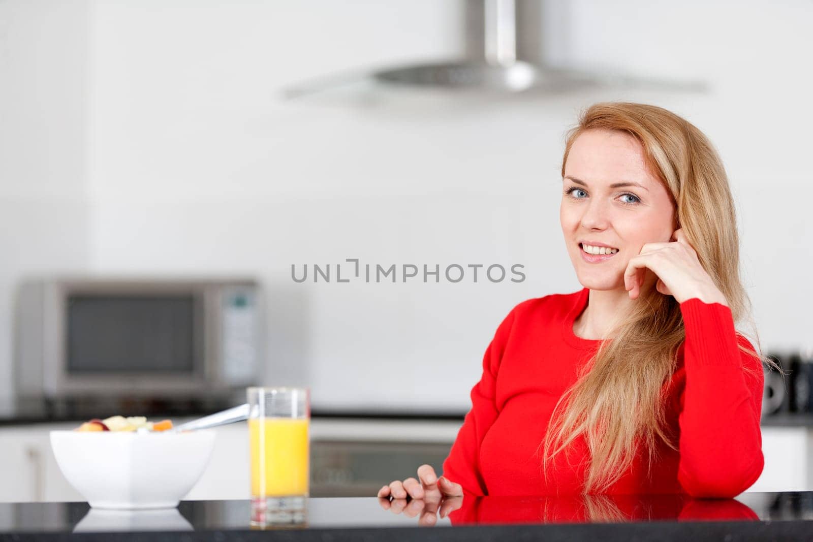 Young woman enjoying a bowl of fresh fruit in her kitchen with orange juice