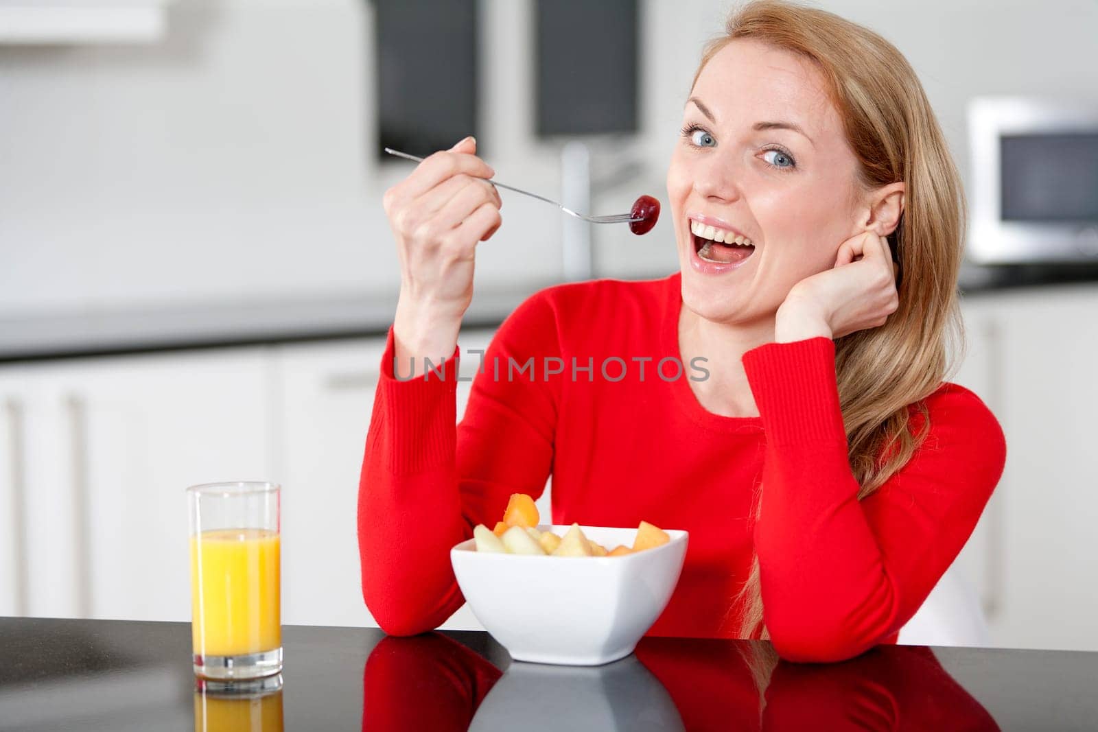 Young woman enjoying a bowl of fresh fruit in her kitchen with orange juice