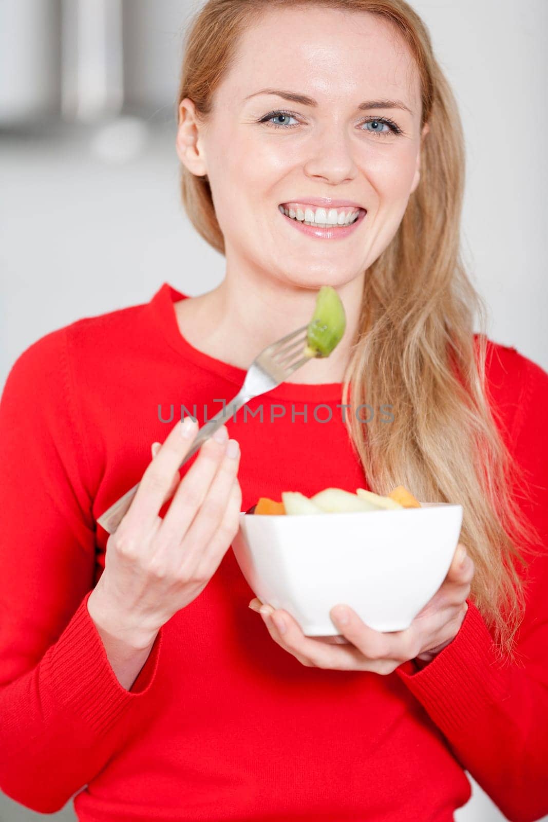 Young woman enjoying a bowl of fresh fruit in her kitchen
