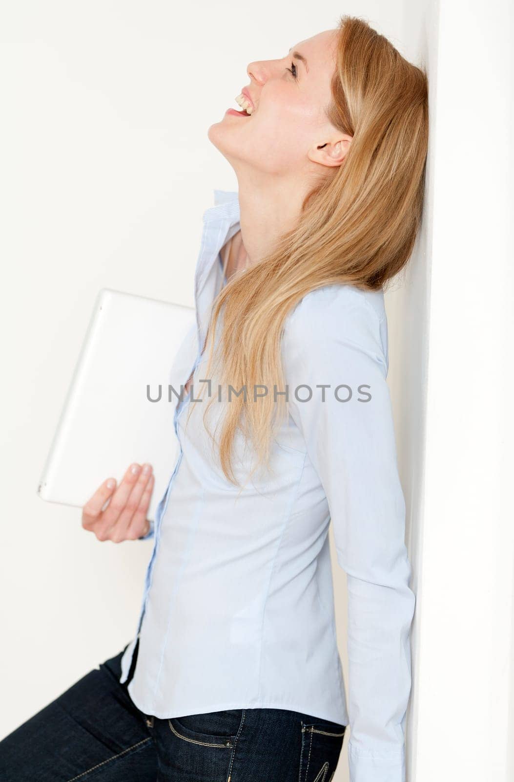 Young woman leaning against a white wall holding a white laptop computer