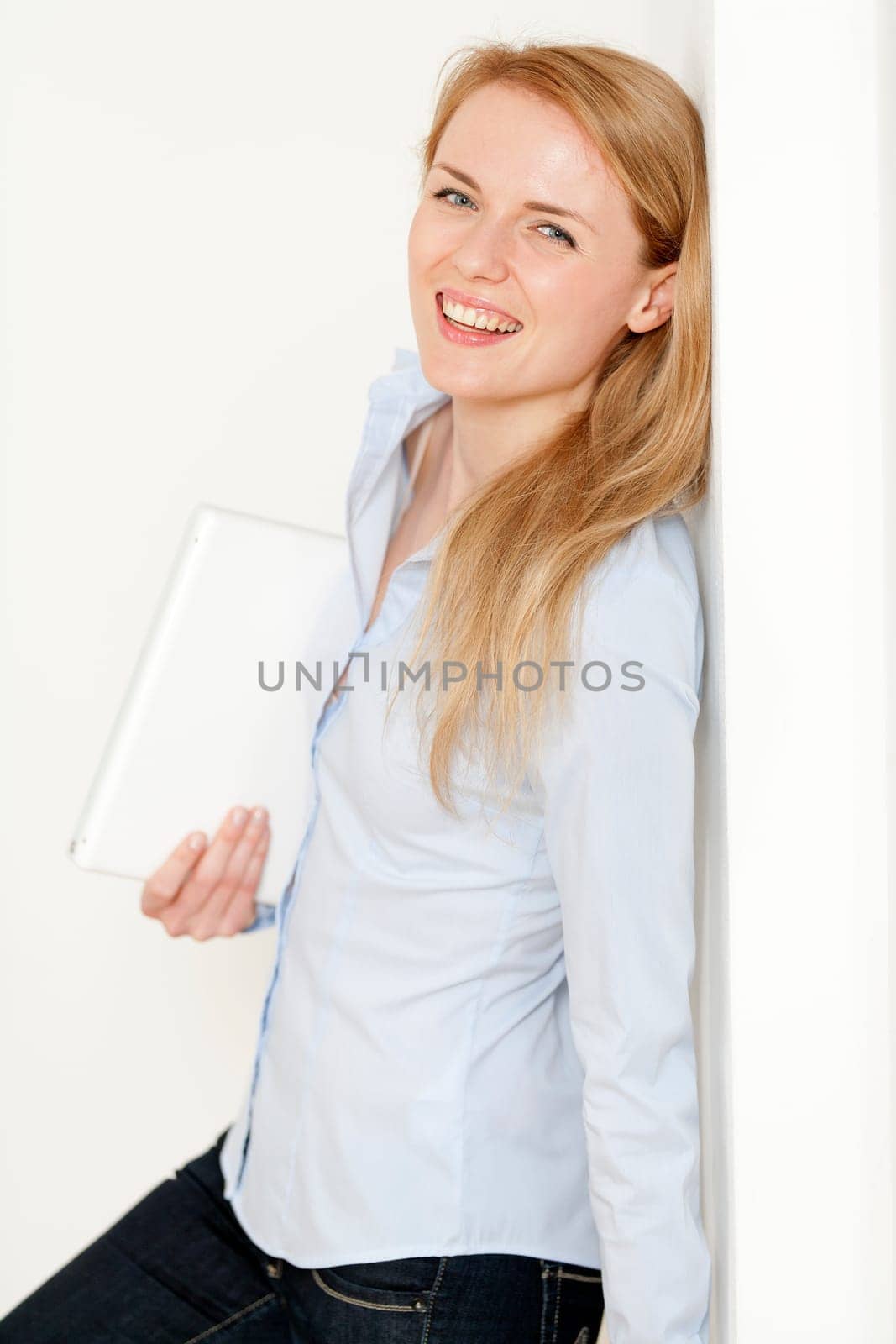 Young woman leaning against a white wall holding a white laptop computer