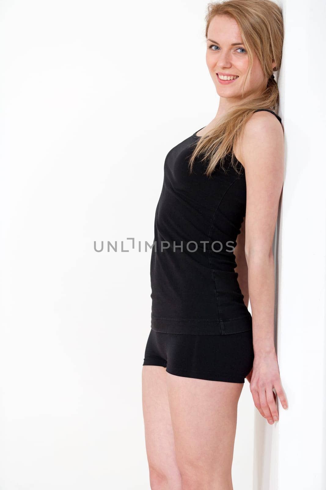 Young woman at home leaning against a white wall in black fitness wear.