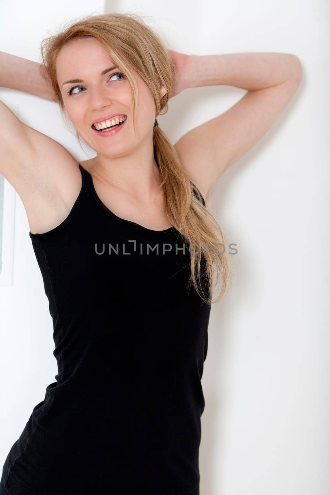 Young woman at home leaning against a white wall in black fitness wear.