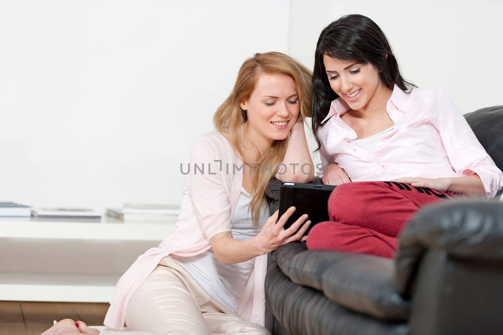 Two woman in their sitting room chatting and having fun on an electronic tablet