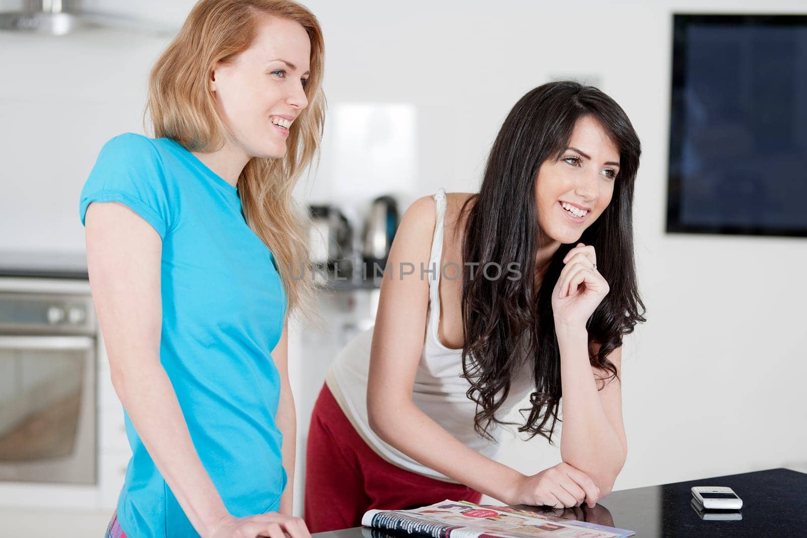 Two young woman chatting and sharing a magazine