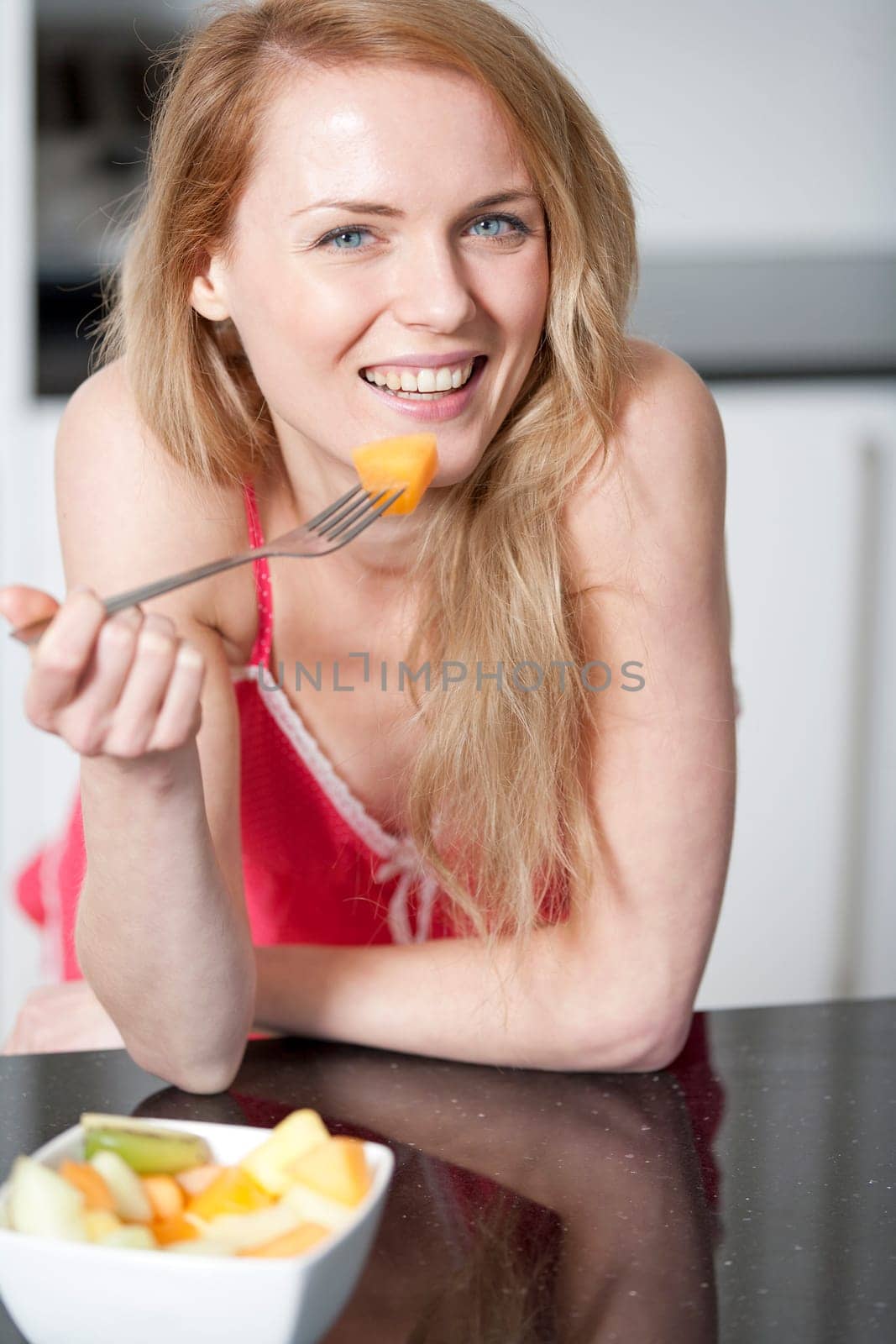 Young woman wearing pink knighty in kitchen eating breakfast