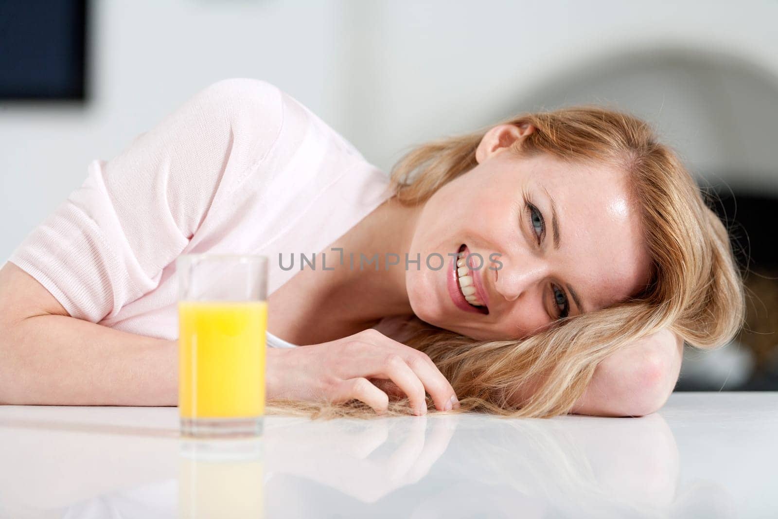 Young woman in pink shirt sitting at dining table at home with orange juice