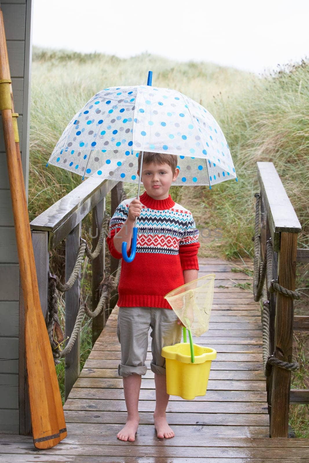 Boy standing on footbridge with umbrella