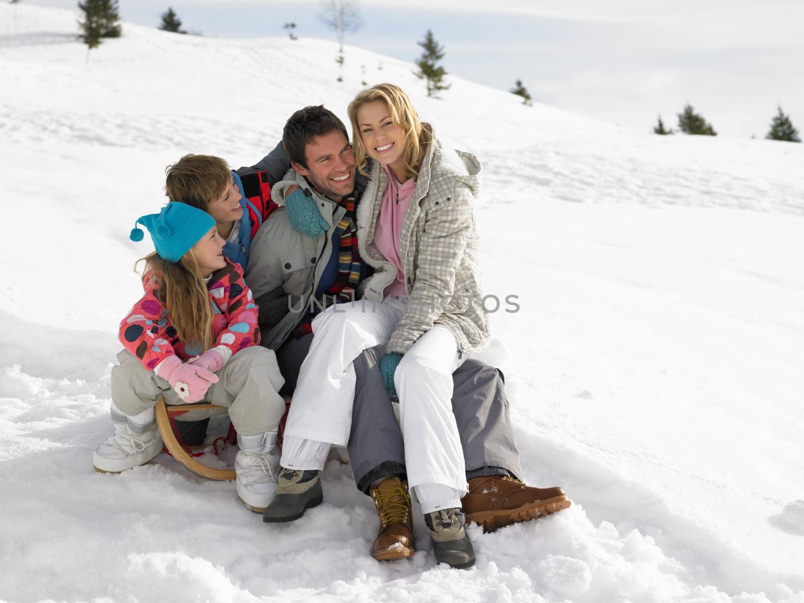Young Family Sitting On A Sled In The Snow