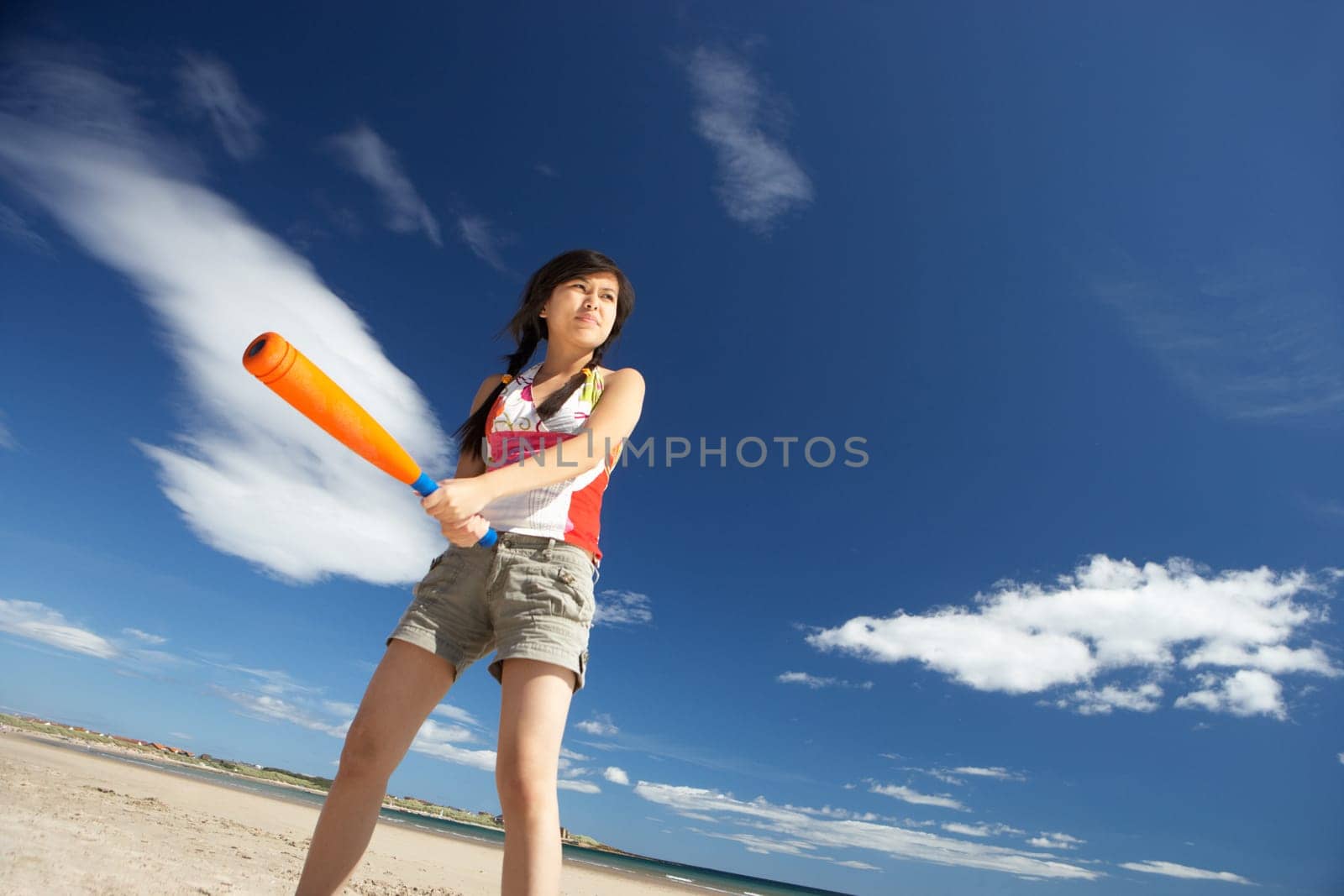 Teenage girl playing baseball on beach