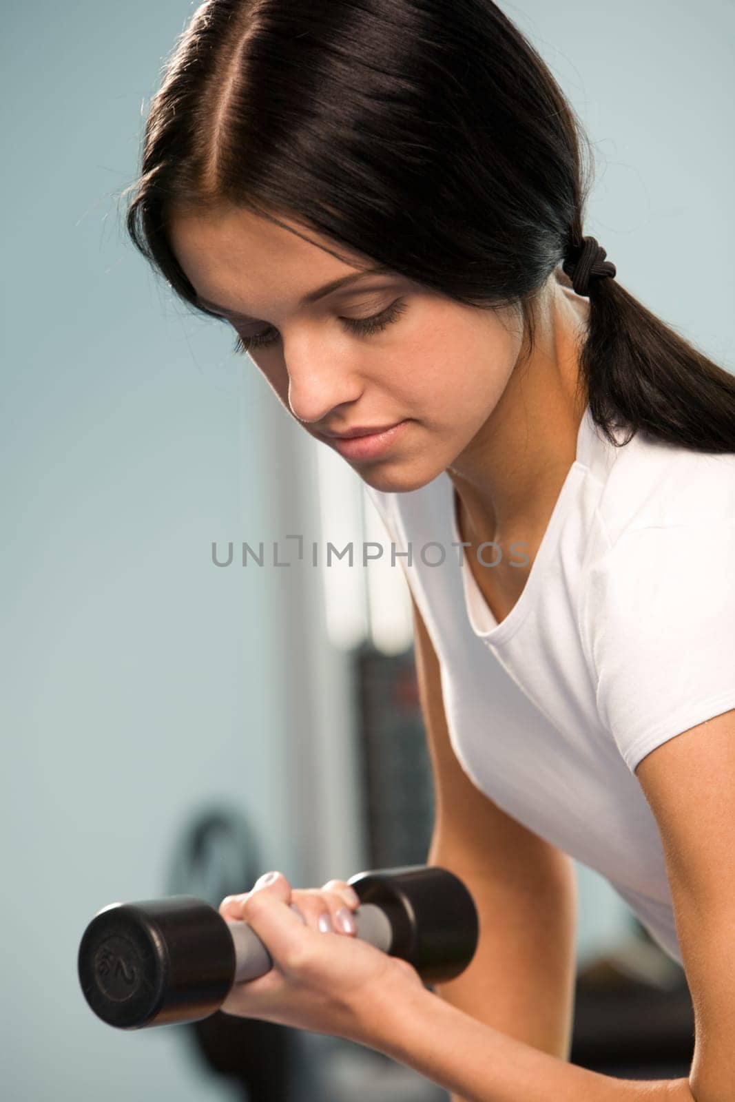 Close-up of sporty girl lifting barbell in left hand in the sportive club