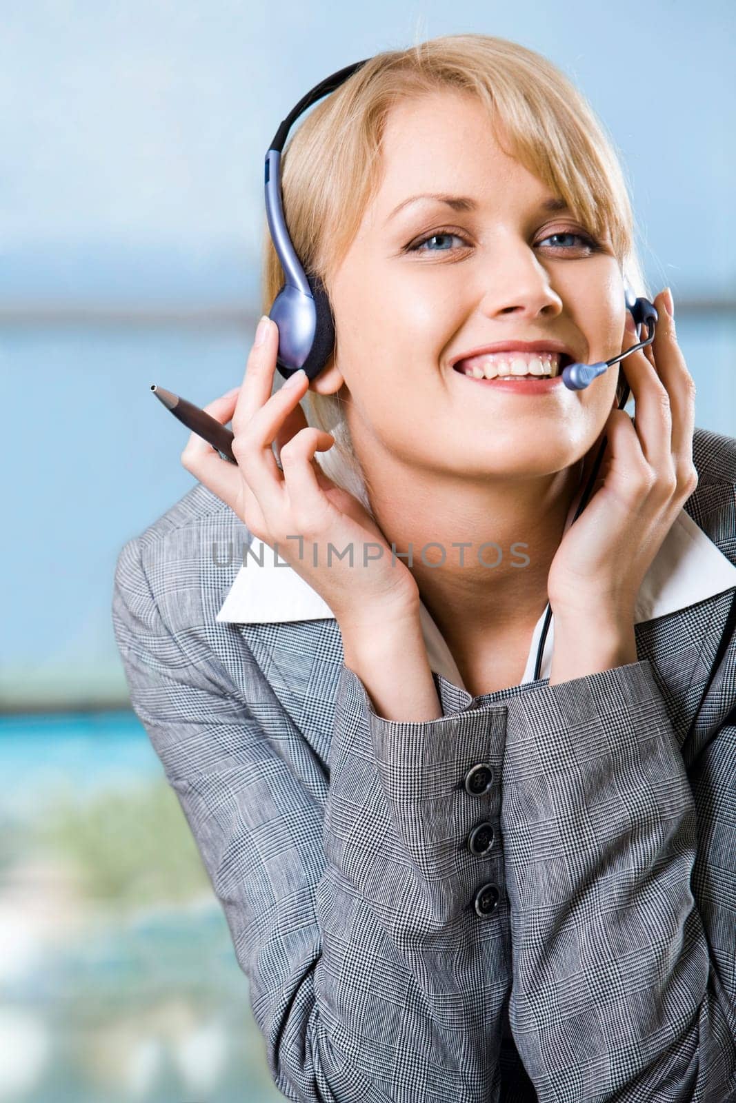 Portrait of beautiful smiling blond businesswoman in gray suit touching headset on her head in front of opened laptop