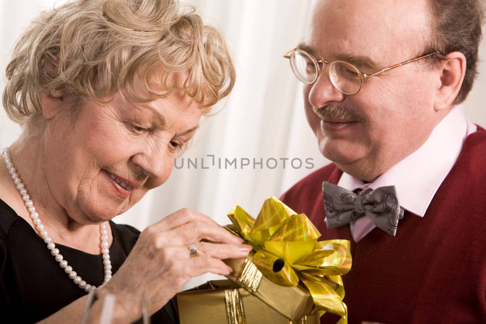 Image of aged woman opening giftbox with her husband near by