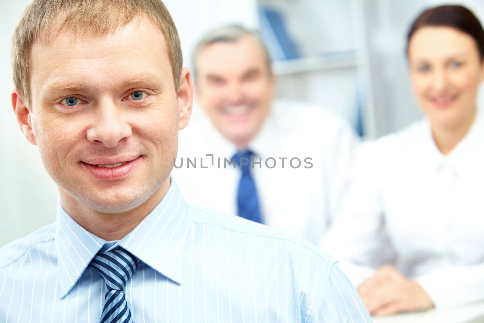 Face of happy businessman looking at camera with two partners on background