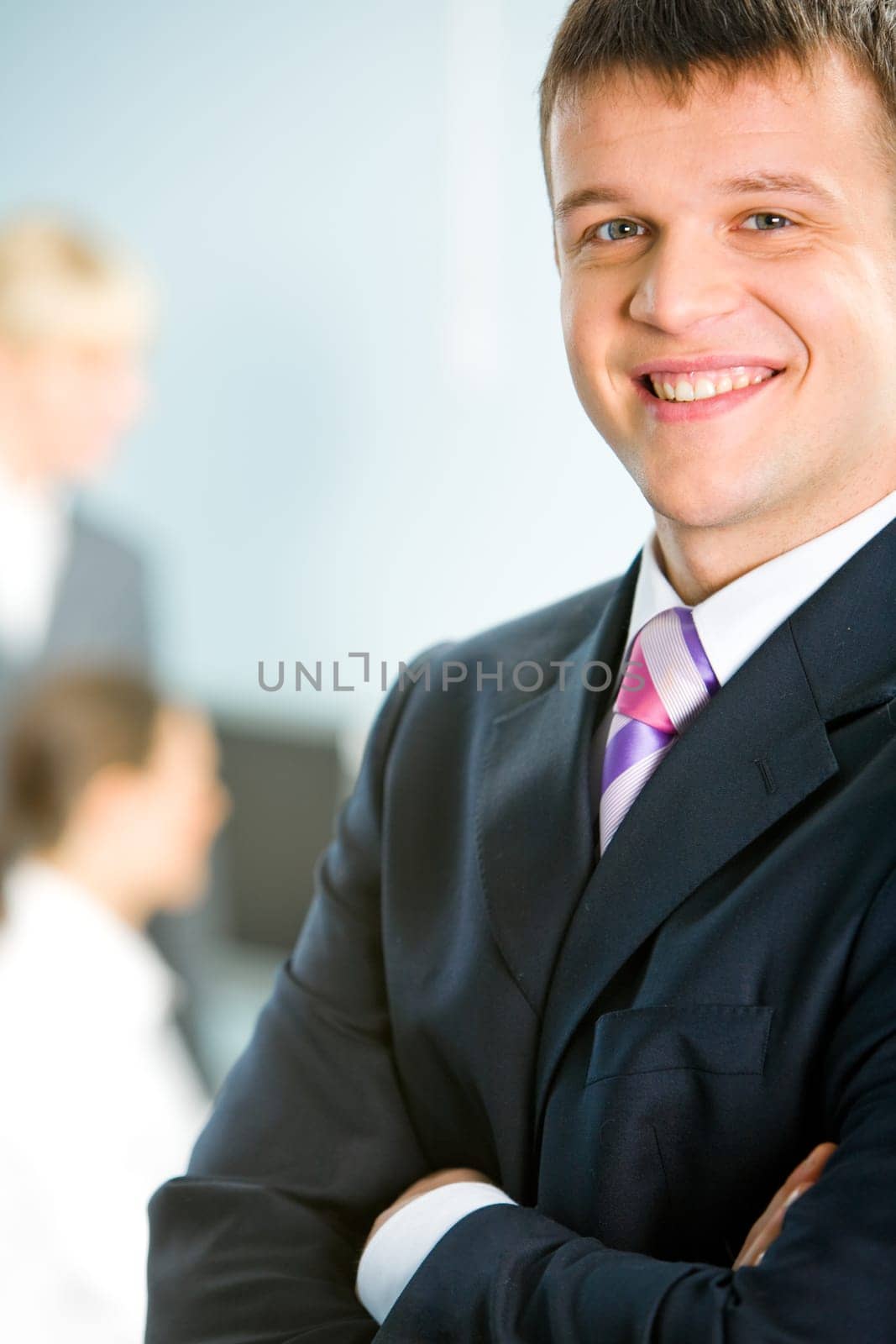 Portrait of a smiling handsome man folding his arms on the background of two business ladies