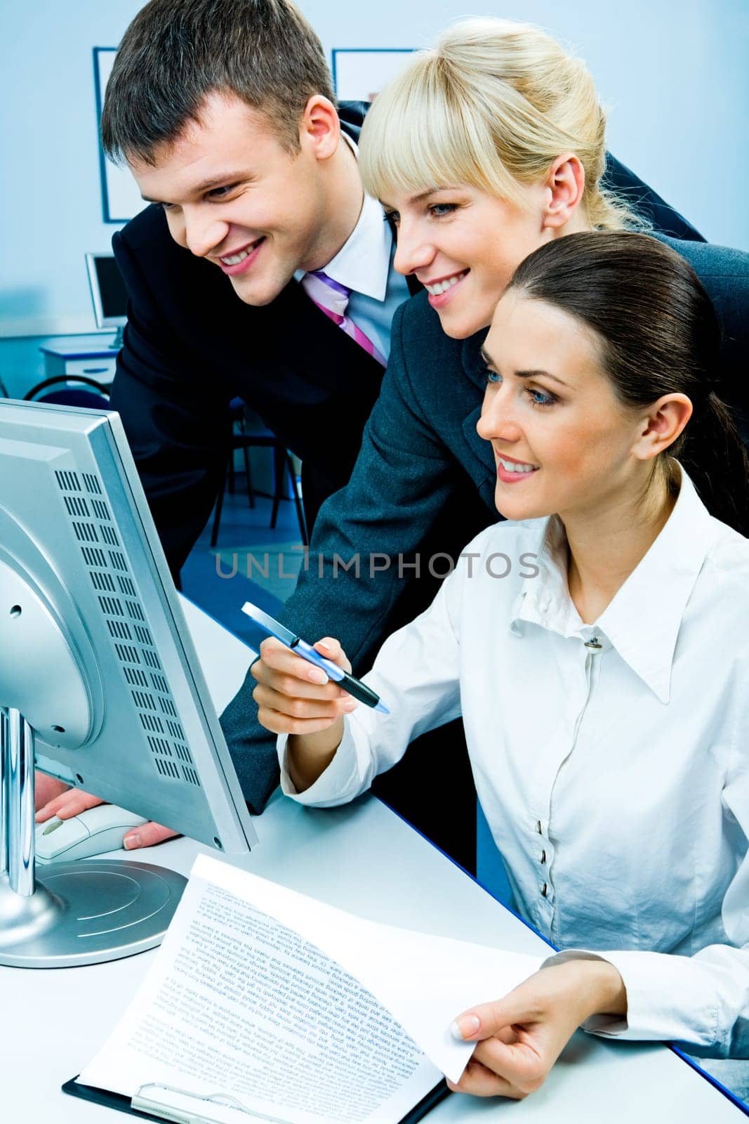 Businessteam of three smiling people looking at the monitor in the computer room