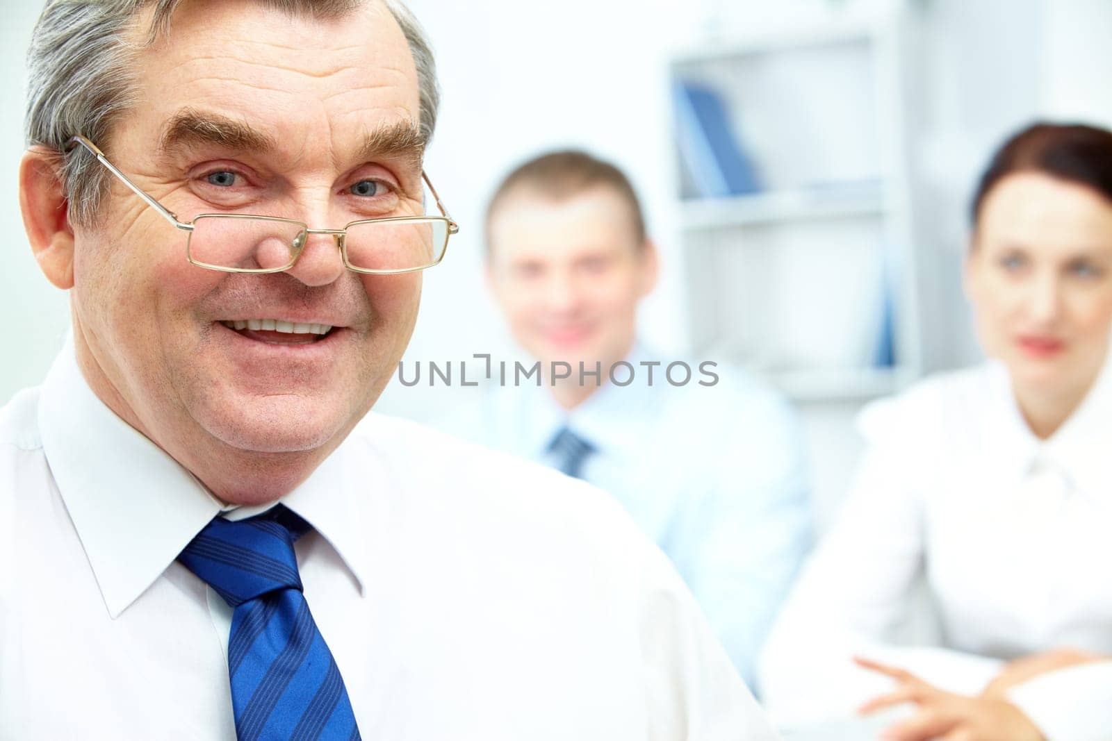 Face of senior businessman looking at camera with two partners on background