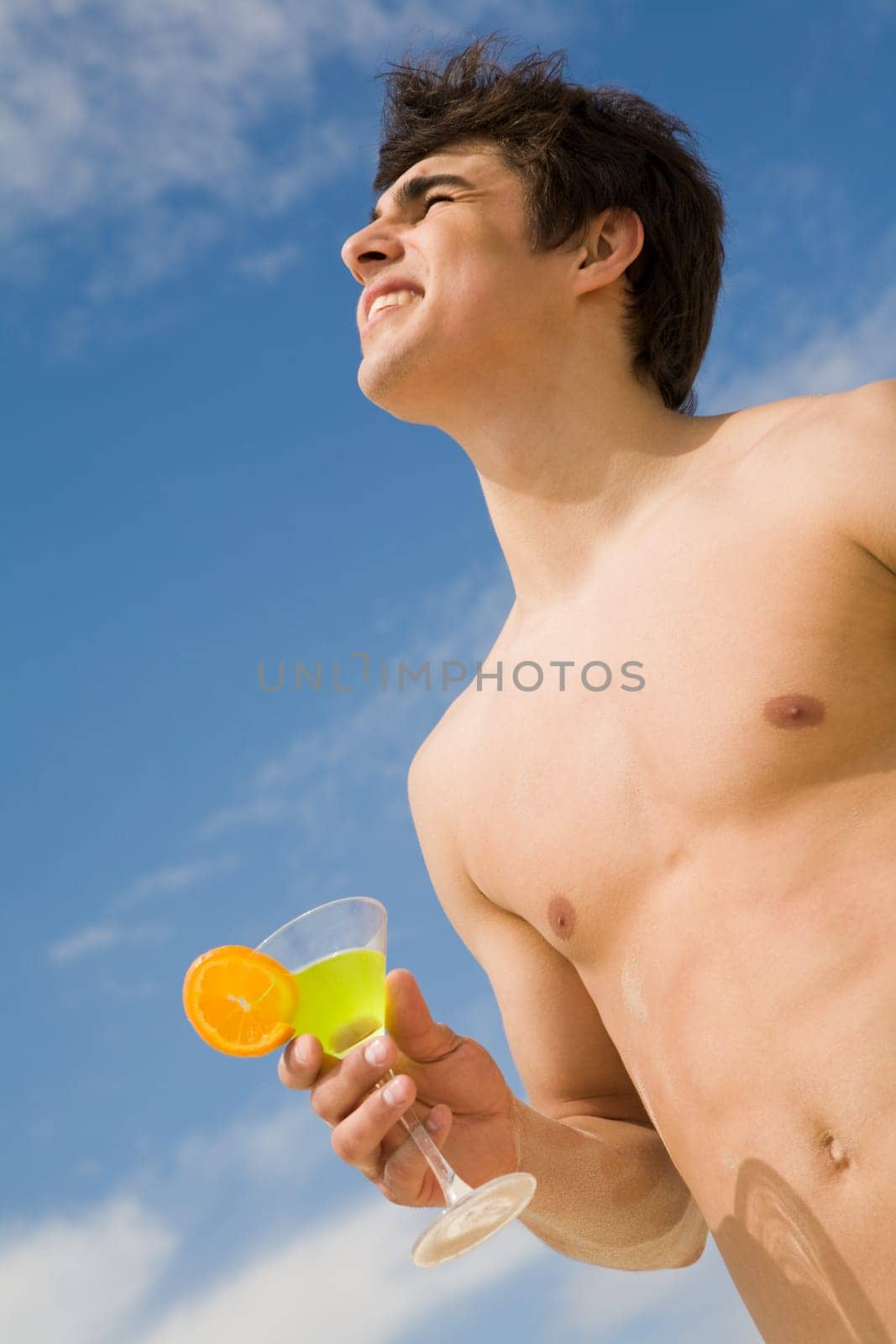 Below view of handsome lad holding martini glass and looking upwards at blue sky