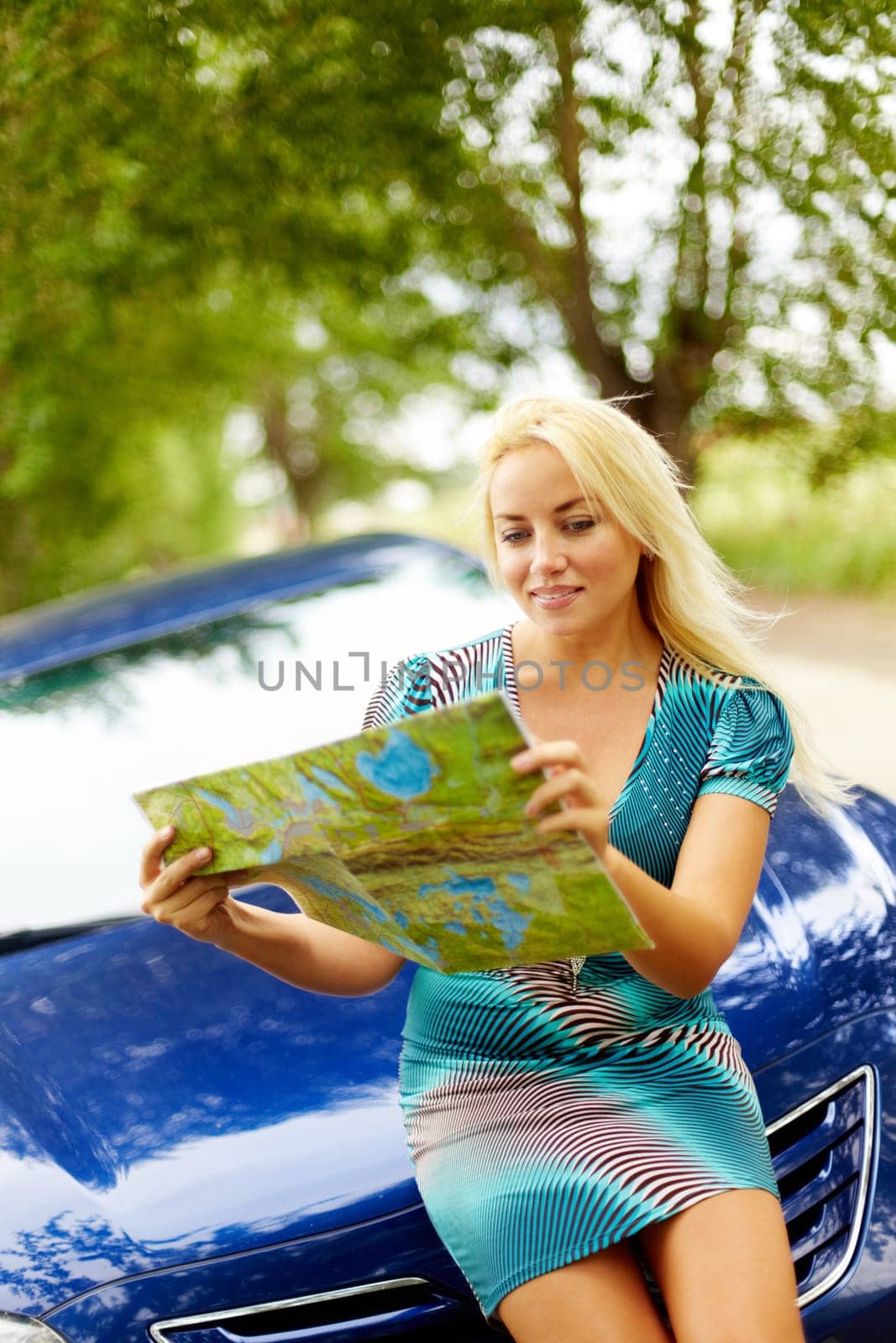 Photo of elegant woman sitting on the hood of car and looking at map