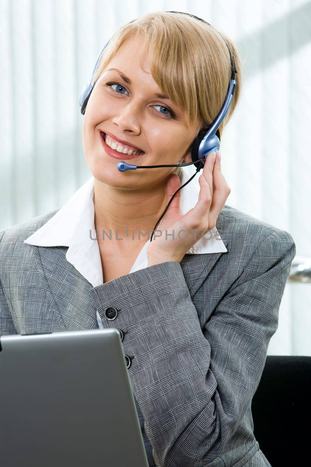 Portrait of beautiful smiling blond businesswoman in gray suit holding a pen in her hand and touching headset