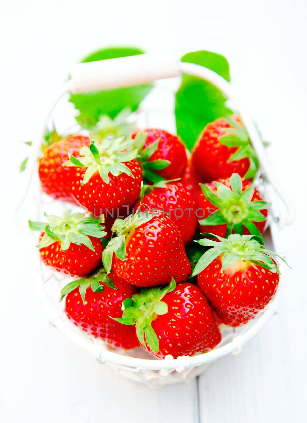 White basket of luscious juicy ripe red freshly picked strawberries on a wooden table