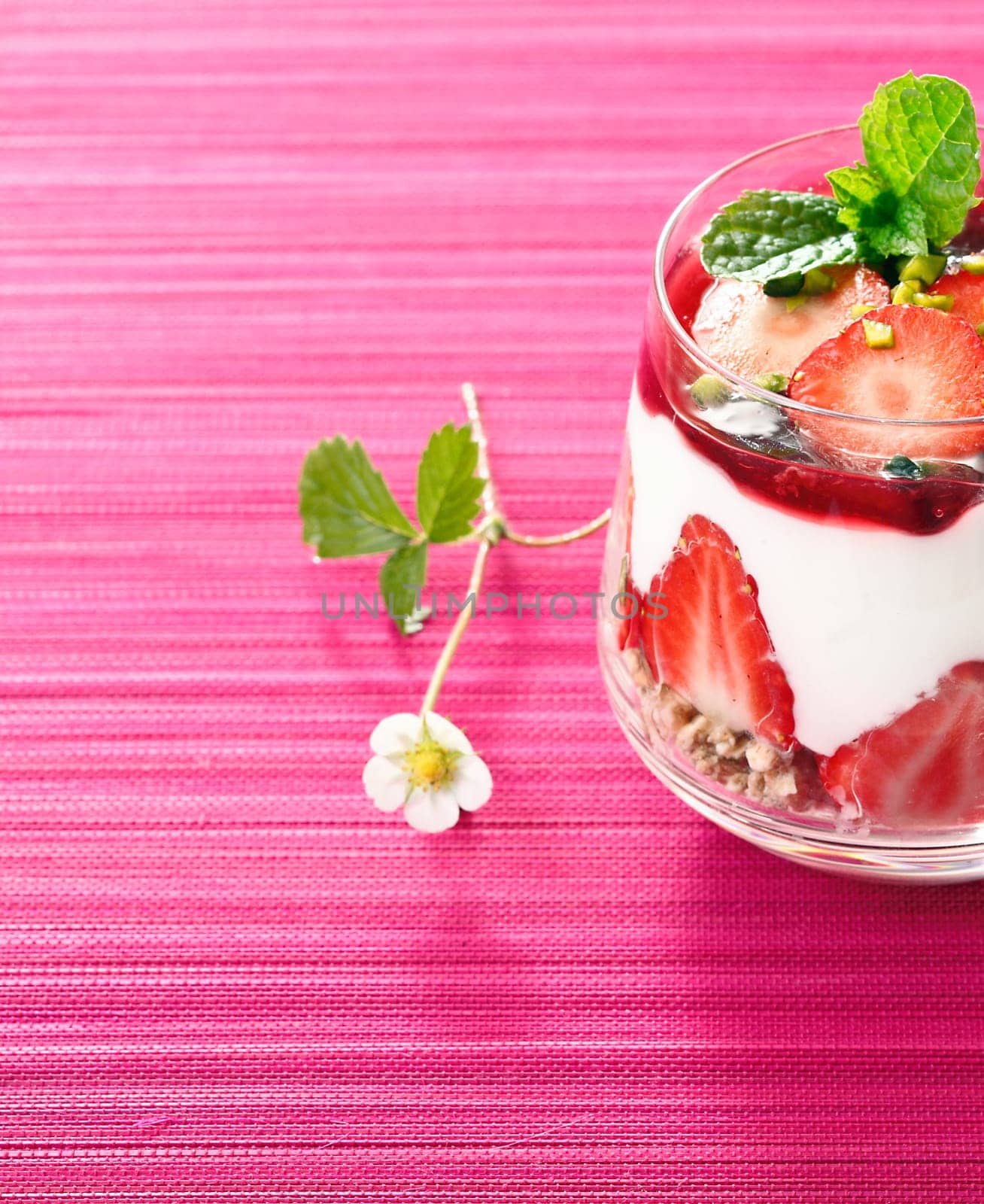 Individual serving of a gourmet strawberry dessert with layered cream alternating with fresh fruit and pudding in a glass container with copspace