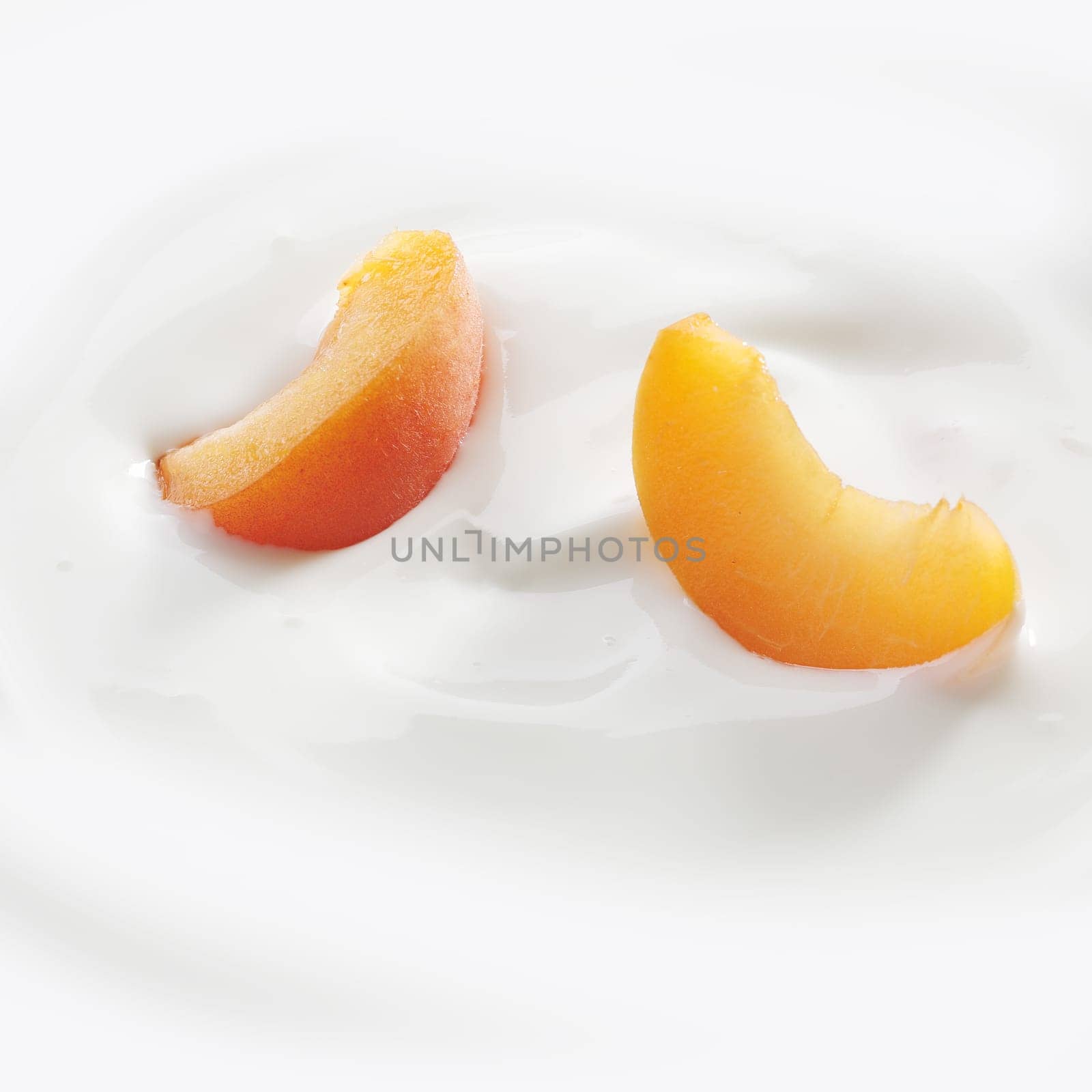 Fresh cut peach slices lay lightly on a fresh serving of yogurt