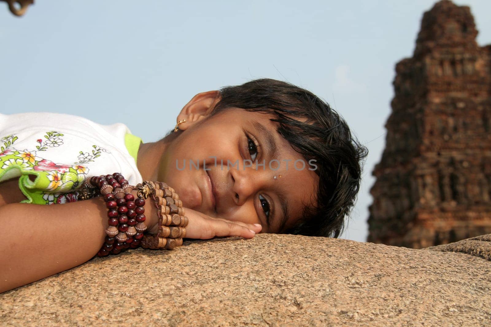 Girl child with ornamental hand bands enjoying rocky lap at Vijayavithala temple in Hampi, Karnataka, India, Asia